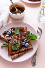Homemade chocolate crepes served with blueberries, sauce and mint leaves on pink background. Selective focus. Top view. Copy space