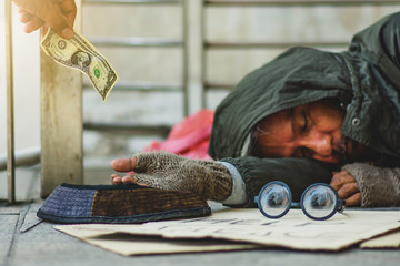 Old homeless man he's sleeping and stretching hand for get a dollars bill from some people. Selective focus at dollars bill.