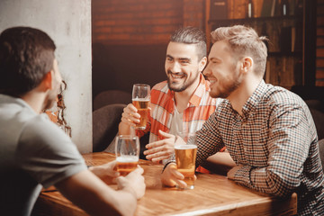 Group of cheerful friends sit in bar with male company, drink beer, laugh