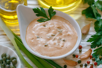 Homemade traditional French remoulade sauce in a White bowl with ingredients-capers, parsley, green onion, mustard, fragrant vinegar, olive oil, garlic on a light wooden table. dip. Selective focus - 249114906