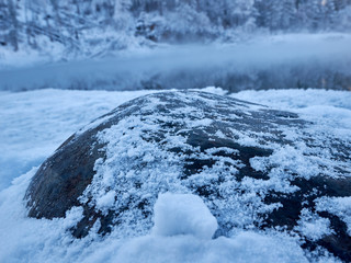 Snow-covered stones and banks with ice edge of the winter river on a cloudy day. Severe frosty winter day Altai region.