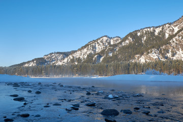Mountain lake. Blue water and large dark stones surrounded by snow-capped mountains Blue sky. Frosty day.