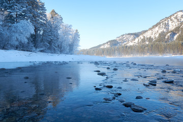 Mountain lake. Blue water and large dark stones surrounded by snow-capped mountains by fields. Blue sky.