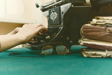 above the keys of an old typewriter female fingers. On the green cloth of the table pince-nez and folders - obrazy, fototapety, plakaty