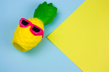 top view summer vibrant blue and yellow  background with funny pineapple toy in sunglasses, copy space