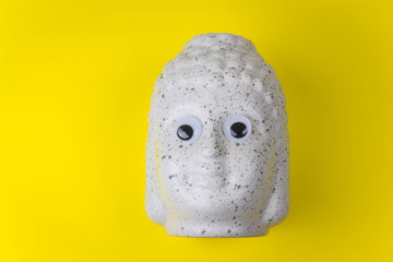Buddha ceramic head with googly eyes on a yellow background