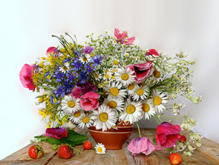 Still life of field daisies and different flowers in a clay vase and a basket with berries on the table
