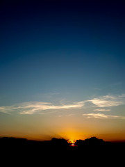 A portrait of a beautiful sunset with a sky with graduated colors from black in the top, blue in the middle and orange in the base and a almost hidden sun