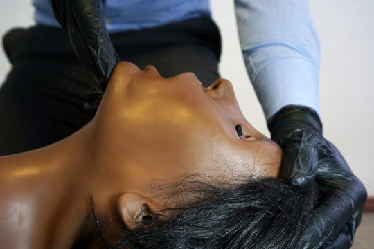 Medical stuff in a black gloves performing 'clear and open tha airway' head tilt - chin lift on a simulation mannequin dummy during basic life support to control the airway.  Medical manipulation