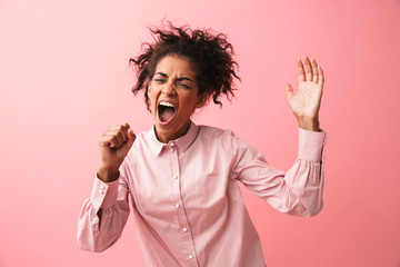 Beautiful young african woman posing isolated over pink wall background screaming singing.