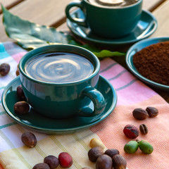Cup with black coffee served outside with raw green, mature red and roasted coffee beans, decorated with green leaves from coffee plant