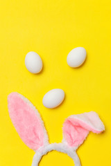 Happy Easter concept. Preparation for holiday. Decorative white eggs and bunny ears furry costume toy isolated on trendy yellow background. Simple minimalism flat lay top view copy space