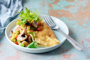 Homemade omelette with mushrooms, vegetables and arugula on a plate. Wonderful healthy breakfast near the window with a cup of coffee.