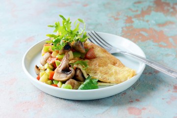 Homemade omelette with mushrooms, vegetables and arugula on a plate. Wonderful healthy breakfast near the window with a cup of coffee.