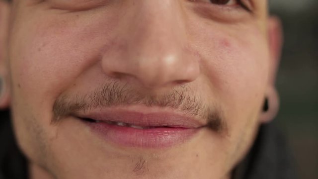Close up shot of smiling young man with thin moustaches.