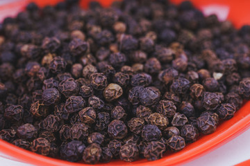 Black pepper in an orange spoon. Spice for delicious food