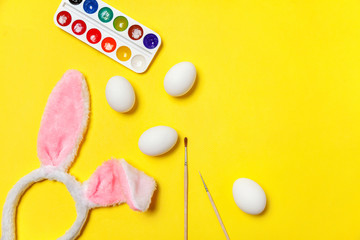 Obraz na płótnie Canvas Happy Easter concept. Preparation for holiday. Decorative eggs colorful paints and bunny ears furry costume toy isolated on trendy yellow background. Simple minimalism flat lay top view copy space