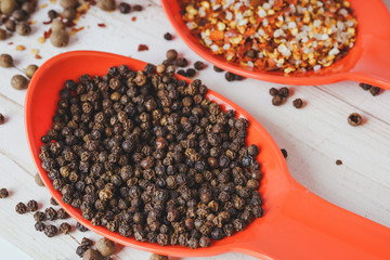 Spices in orange spoon on white wooden background. seasoning delicious food. Paprika, black pepper peas, Gross natural sea salt mixed with dried red hot chili pepper, colorful seasoning close-up