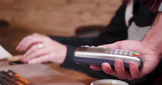 Woman pays for coffee with a contactless credit card. Close up 4K shot