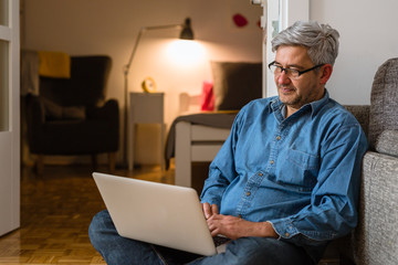 gray haired man using laptop relaxed in his living room