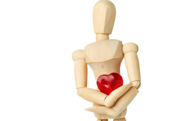 The wooden figure of a man holds in his hands a red heart on a white background. Gives the heart