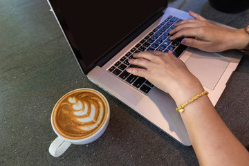 Hands of woman working on laptop computer with latte art coffee cup