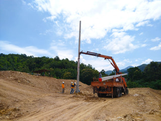 The crane pulls the electric pole into the hole.