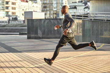 Full of energy! Full length portrait of athletic african man running with very fast speed through the sunny city streets. Side view