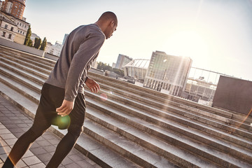 Urban workout. Back side photo of athletic african man in sportswear going upstairs while his morning training
