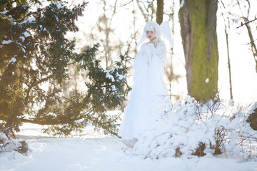 Beautiful girl stands in snowy forest in image of good angel with wings.