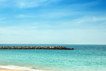 Picturesque view of ocean with rock breakwater on sunny day