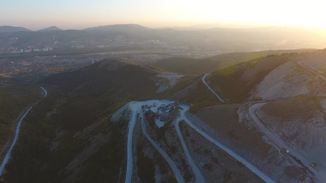 Flying over the mountains. Plant in the mountains. The city is far away. Sunset.