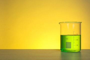 Beaker with liquid on table against color background. Chemistry laboratory glassware