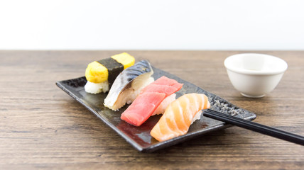 Fototapeta na wymiar Japanese rice balls, various national dishes (salmon, saba fish, eggs, seaweed rolls And red meat fish), sushi arranged on a black plate on a wooden floor