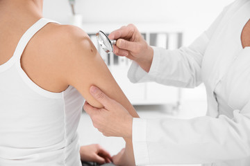 Dermatologist examining patient's birthmark with magnifying glass in clinic, closeup