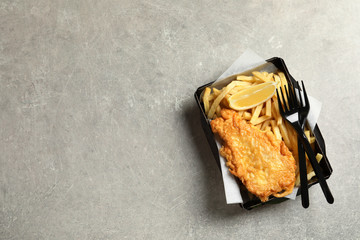 Disposable container with British Traditional Fish and potato chips on grey background, top view....