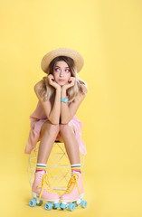 Young woman with retro roller skates on color background