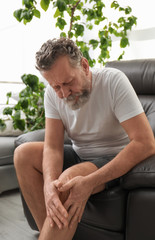 Fototapeta premium Senior man suffering from knee pain indoors