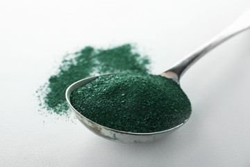Spoon with spirulina algae powder on white background
