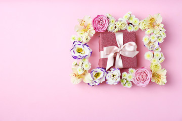 Frame of flowers and gift box on color background, top view. Space for text