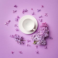 white empty coffee Cup on bright purple background with branches and lilac flowers. copy spase, flat lay