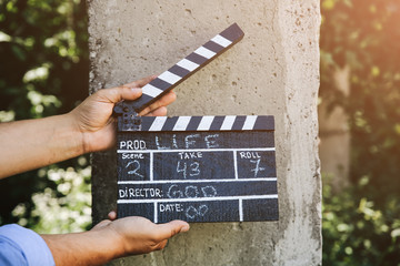 Cool hipster guy is holding in his hands a black clapperboard on concrete background. Man is...