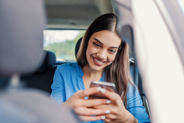 Beautiful woman smiling while sitting on the front passenger seats in the car. Girl is using a smartphone