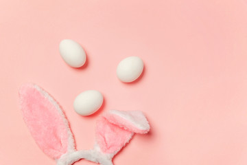 Happy Easter concept. Preparation for holiday. Decorative white eggs and bunny ears furry costume toy isolated on trendy pastel pink background. Simple minimalism flat lay top view copy space