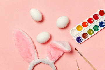 Happy Easter concept. Preparation for holiday. Decorative eggs colorful paints and bunny ears furry costume isolated on trendy pastel pink background. Simple minimalism flat lay top view copy space