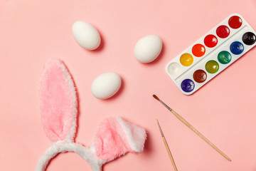 Happy Easter concept. Preparation for holiday. Decorative eggs colorful paints and bunny ears furry costume isolated on trendy pastel pink background. Simple minimalism flat lay top view copy space