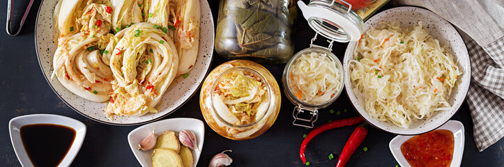 Fermented food. Vegetarian food concept. Cabbage kimchi, tomatoes marinated, sauerkraut sour glass jars over rustic kitchen table. Canned food concept. Top view. Banner. Flat lay