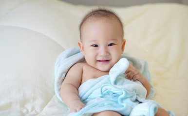 Happy baby in a blue towel sitting on bed after bathing