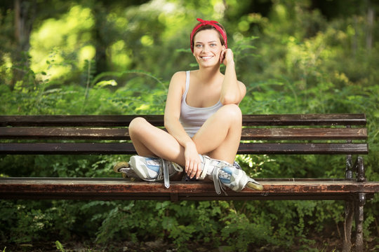 Young beautiful happy woman with inline skates on bench posing for a camera