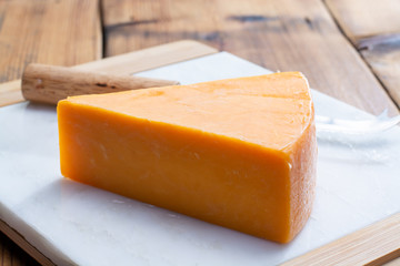 Piece of bright yellow hard cheese cheddar, originating in the English village of Cheddar in Somerset - obrazy, fototapety, plakaty